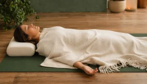 Woman in supported savasana with a thick blanket covering the body and a pillow under the head, safe environment